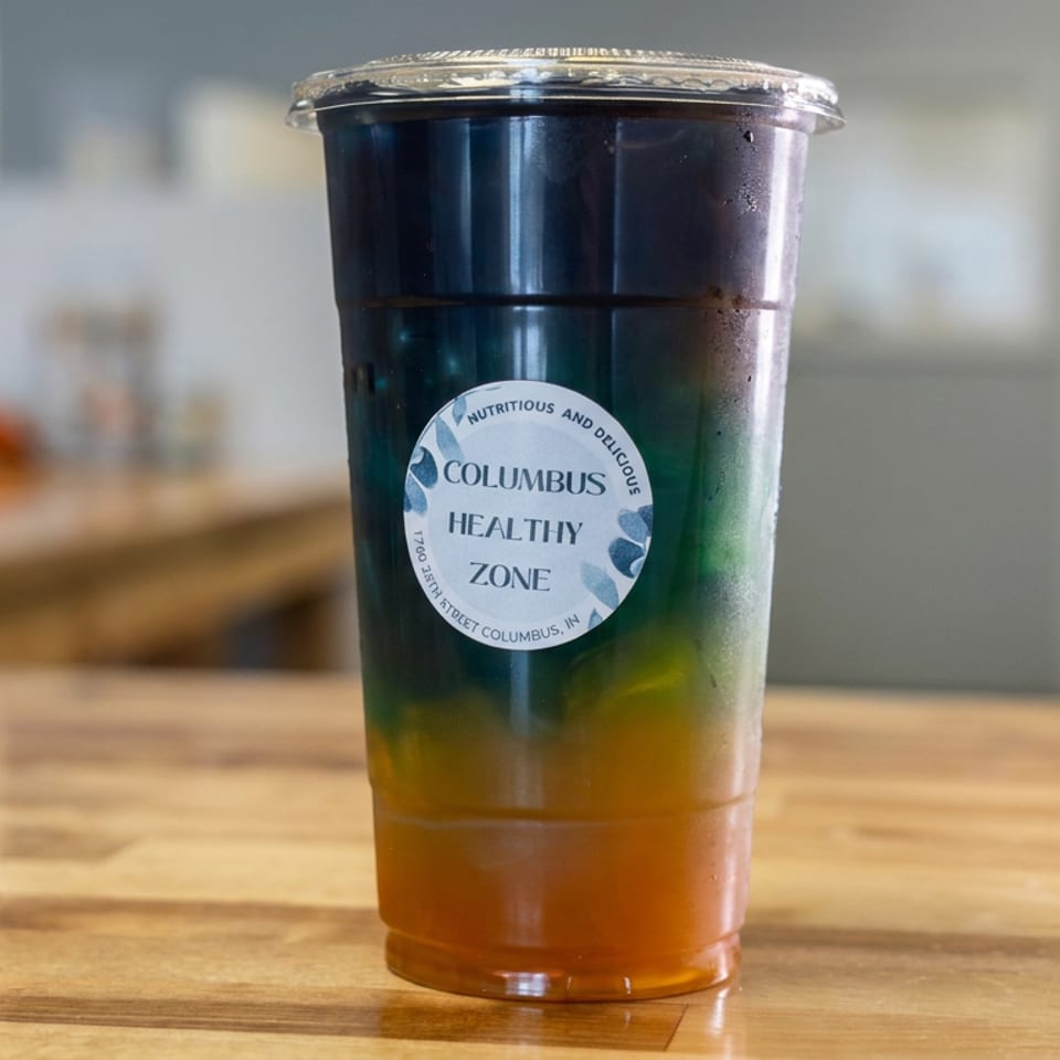 Clear plastic cup of layered green and orange juice labeled Columbus Healthy Zone on a wooden table.